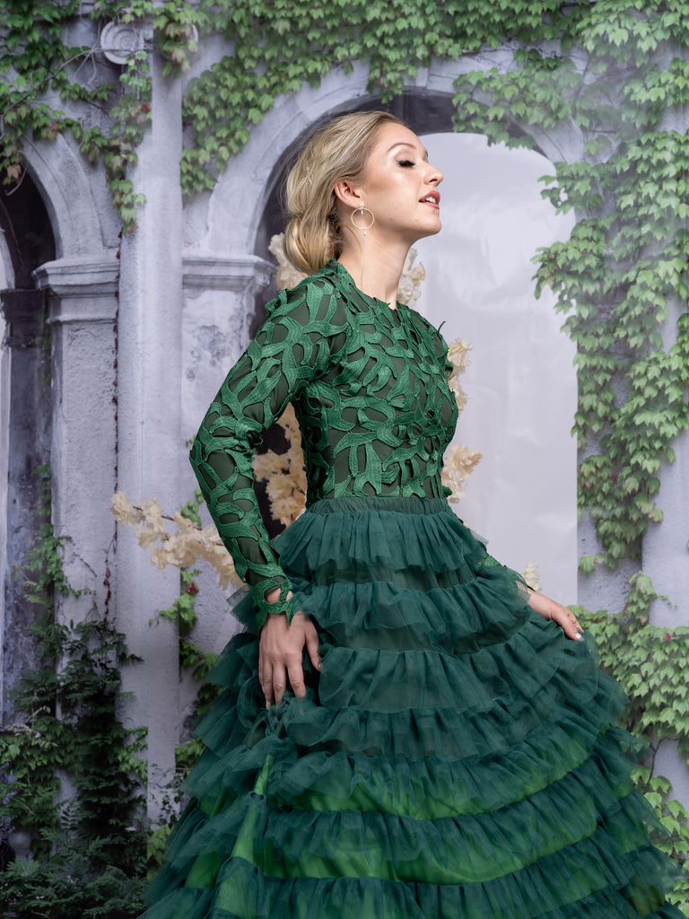 A woman wearing a modest ombre green tiered gown with long sleeves. The gown has a fitted bodice and multiple tiers of ruffles.