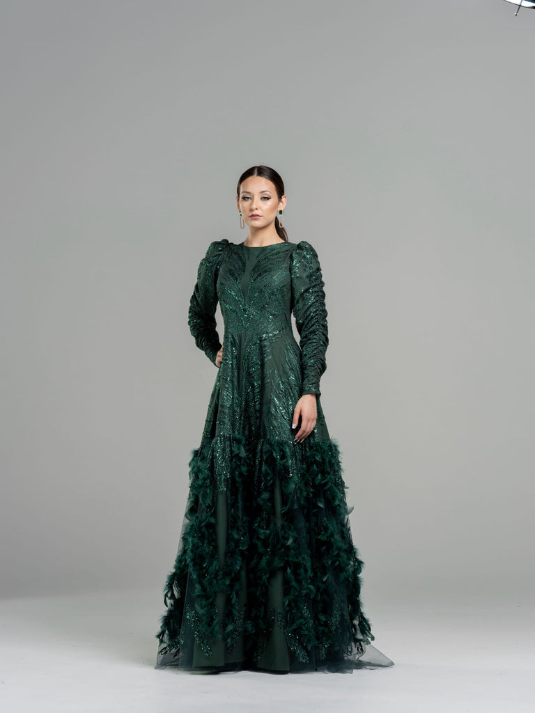 Woman wearing a hunter green sequin drop waist gown with a dramatic feather bottom detail.