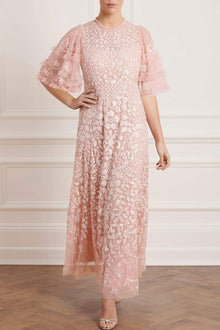  Woman wearing modest Needle & Thread Aurelia Gown in pink strawberry icing color. The gown is adorned in light pink sequin detailing and has three-quarter flare sleeves.