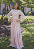 Woman wearing a modest blush pink gown with a butterfly top and an accordion pleated bottom. The delicate pink color and intricate pleating add a romantic and playful touch to the gown.
