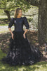 Woman wearing modest black tiered ball gown. The gown features three-quarter sleeves with puff sleeve detail. 