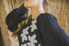 Woman wearing a black modest boho style gown with long sleeves and white beaded flowers cascading down one side.