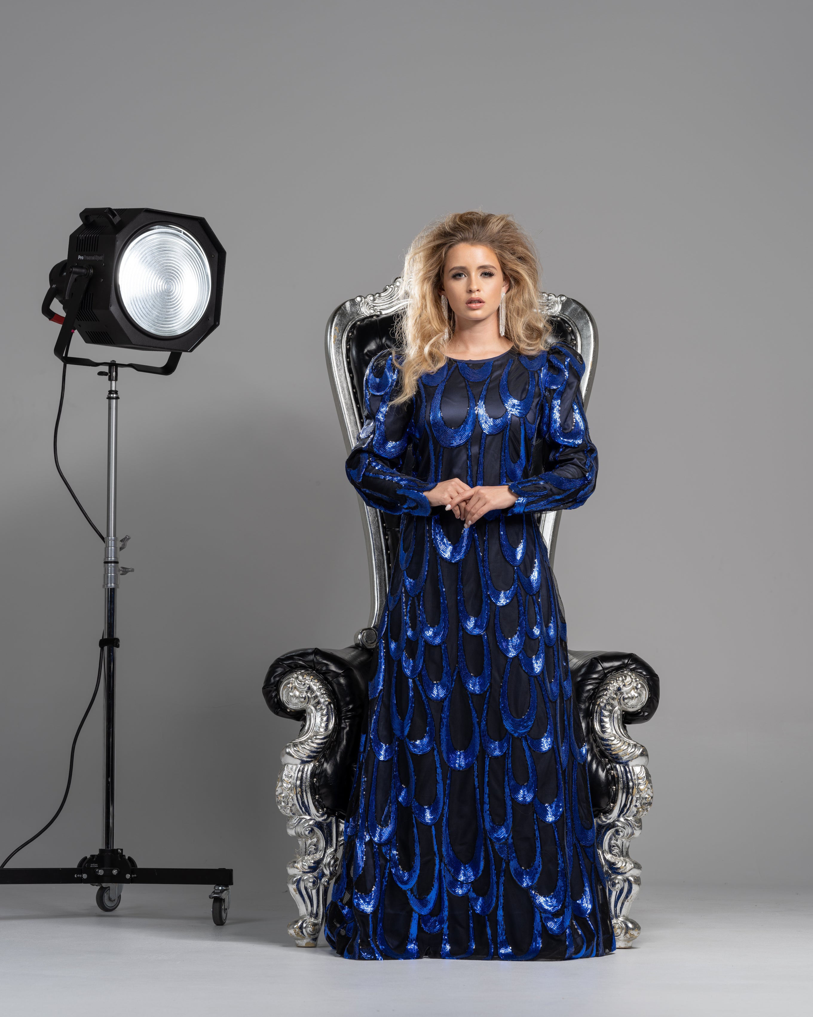 A woman wearing a modest black and cobalt gown with a simple, flattering silhouette made from a shimmering cobalt blue sequin fabric.