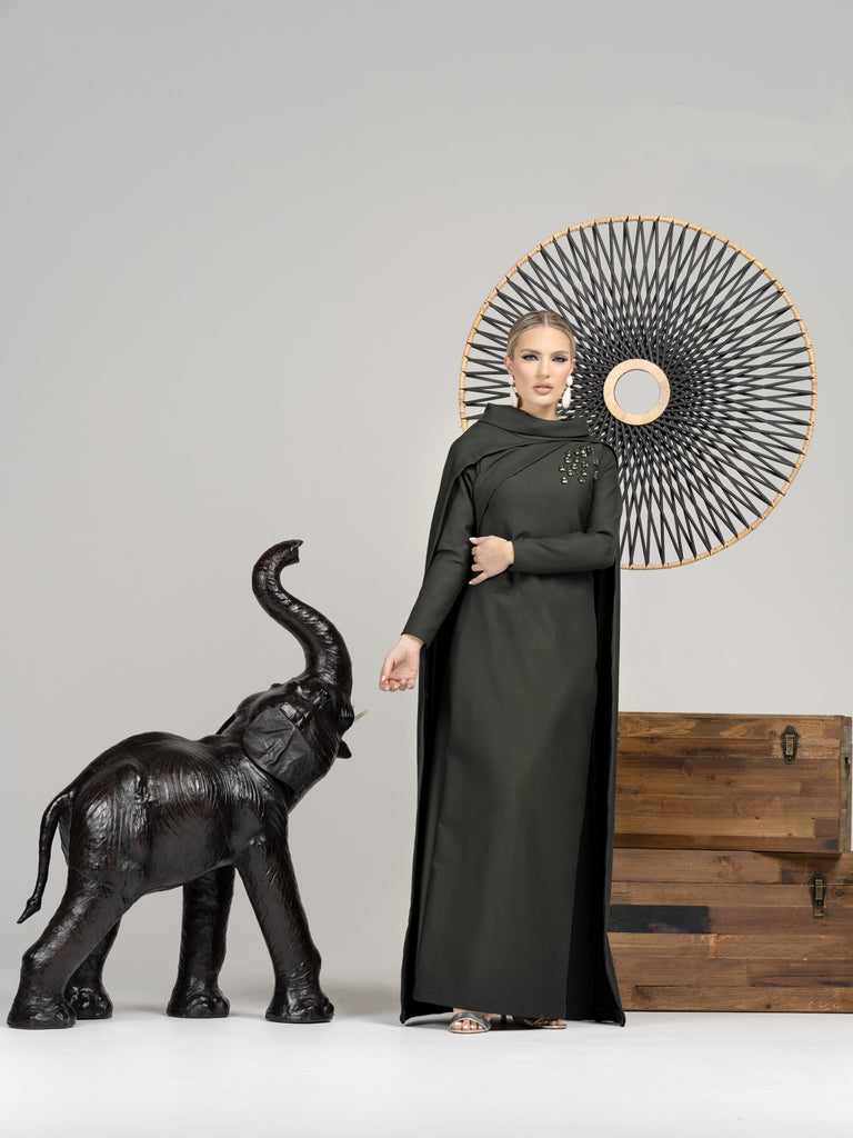 Woman wearing modest hunter green straight silhouette gown with cape in back.