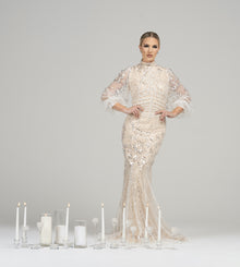  Woman wearing modest champagne beaded straight gown with a high neck and three-quarter length bubble sleeves. The gown has a slim silhouette and is adorned with sparkling beadwork. 
