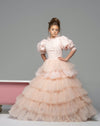 A girl wearing a modest blush pink ball gown with puff sleeves and a floral top. The gown has a tiered ball gown skirt.