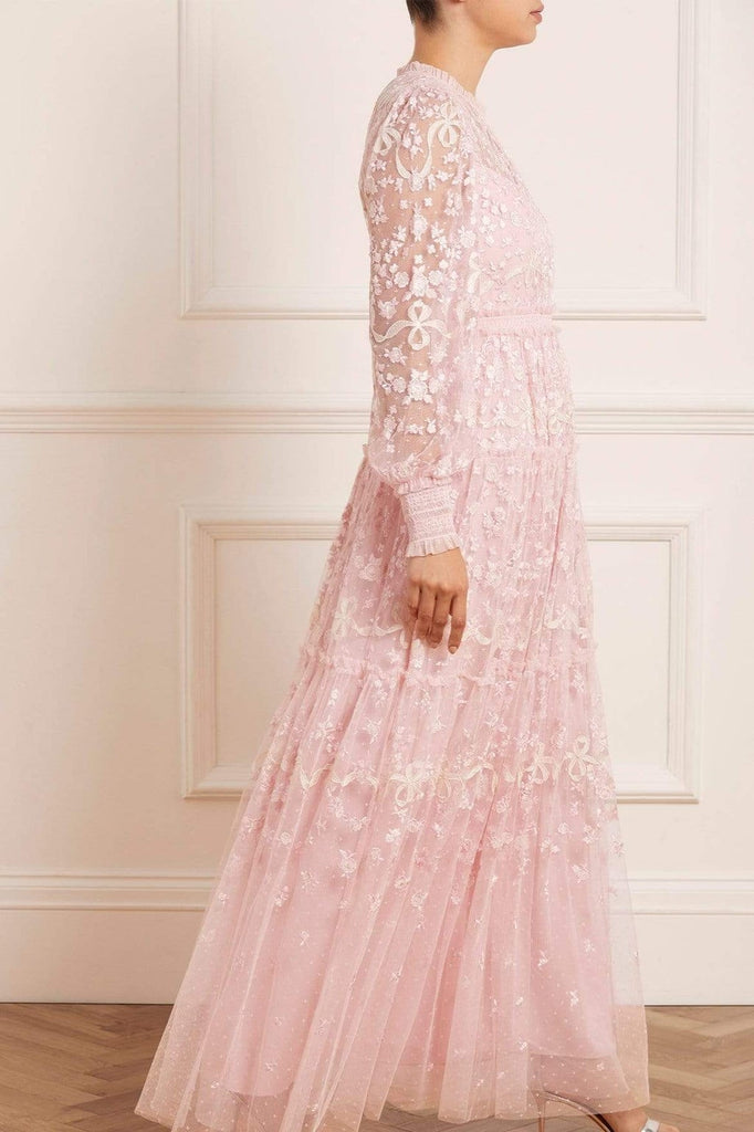A woman wearing a modest ballerina pink Needle & Thread Emiliana Gown. The gown is made from a soft and flowy fabric and has a feminine and romantic feel.
