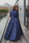 Woman wearing modest cobalt blue and black ball gown with cropped bolero. The three-quarter sleeve bolero has a large bow detail in front and mini covered buttons cascading down the back.