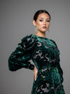 A woman wearing a modest dark green floral velvet burnout gown with puff sleeves. 
