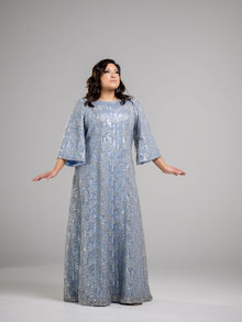  A woman wearing a plus size sky blue modest gown with a silver honeycomb overlay and flare sleeves.