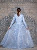 Woman wearing a modest powder blue floral long sleeve gown with a flowing skirt cape for added elegance.