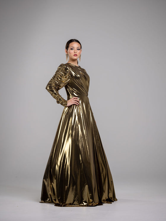 A woman wearing a golden ruched gown with long sleeves. The gown has a fitted bodice and a flowing skirt.