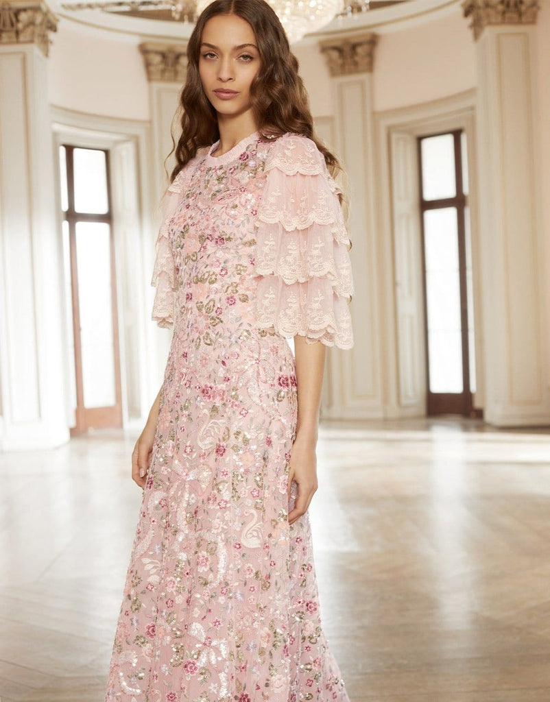Woman wearing a modest blush pink Needle & Thread Odette Ballerina Dress gown with beaded floral embellishments and three quarter flare sleeves. 