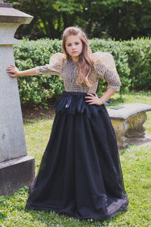  Girl wearing modest black gown with gold top overlay cut from glamorous mini sequin and glitter, and voluminous puffed sleeves. Black feather peplum waist detail.