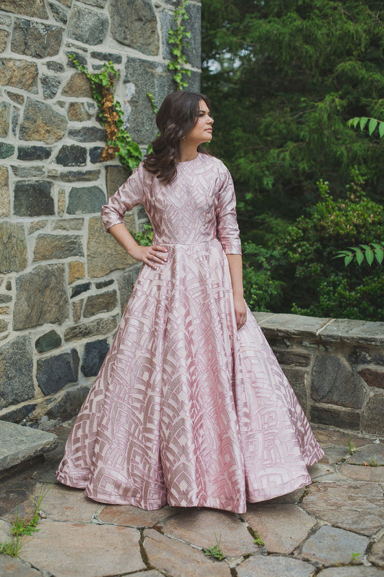 Woman wearing a modest blush pink ball gown with pink foiled geometric shapes and three-quarter length sleeves.