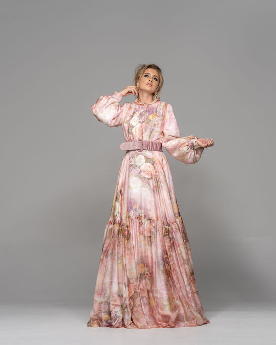 Woman wearing a modest pink floral garden print gown made from silk flowy fabric with a large stretchy buckle mauve belt.