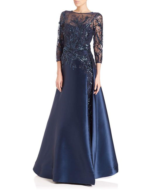 Woman wearing Teri Jon modest navy ball gown with sequined branch detailing on top and waist. 